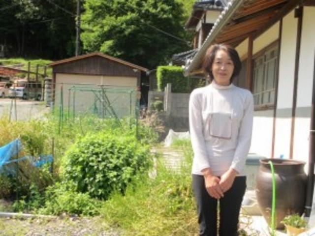 古民家の庭先に立っている笑顔の渡辺さんの写真