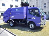 建物の間の芝生の上に停めてある、青いごみ収集車両の写真