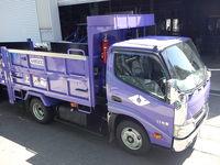 シャッターの前に停めてある、紫のごみ収集車両の写真